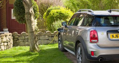 BUCKINGHAMSHIRE, İngiltere - 09 Nisan 2022. Elektrikli araba evde şarj oluyor. Elektrikli Mini Yurttaş evin önüne park etmiş, fişi takılı ve şarj oluyor..
