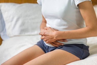 Woman holding stomach with cramp or pain. Female mid adult Asian Indian, UK
