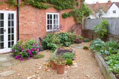 UK garden of Victorian country house in autumn, with gravel, York stone patio, French doors and oak sleeper raised beds.