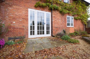 Wooden French doors and a York stone patio in a UK landscaped garden with autumn leaves