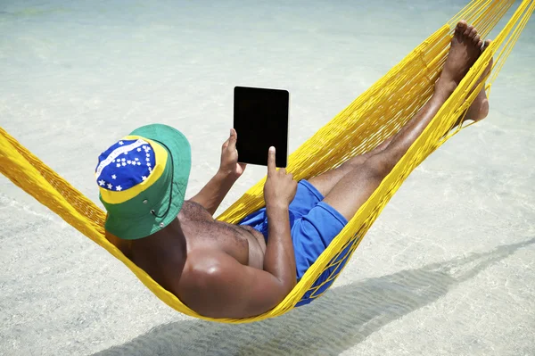 Hombre brasileño se relaja usando tableta en hamaca en la playa — Foto de Stock