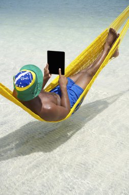 Brezilyalı adam hamak Beach tablet kullanarak rahatlatır