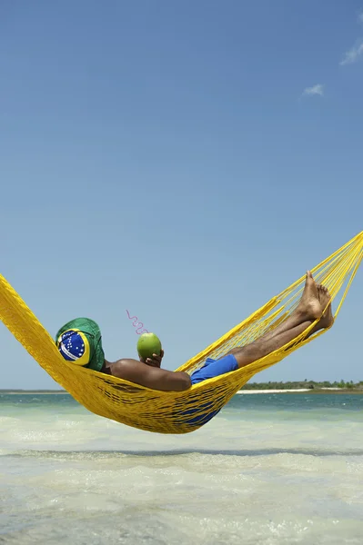 Brasiliansk mann som slapper av i Beach Hammock med å drikke kokosnøtt – stockfoto