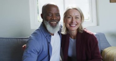 Oturma odasında oturan, kucaklayan ve gülümseyen mutlu yaşlı çift portresi. emeklilik yaşam tarzı, evde zaman geçirme..