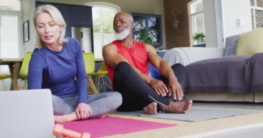 Karışık yarış son sınıf çifti evde dizüstü bilgisayara bakarak esneme egzersizi yapıyor. emeklilik ve aktif yaşlı yaşam tarzı konsepti