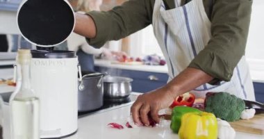 Önlük giyen Afrikalı Amerikalı son sınıf öğrencisi mutfaktaki gübre kutusuna sebze kabuğu koyuyor. emeklilik son sınıf yaşam tarzı konsepti