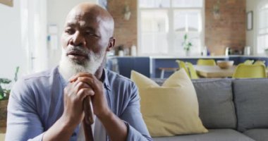 Oturma odasında kanepede oturan, baston tutan düşünceli kıdemli Afrikalı Amerikalı adam. emeklilik yaşam tarzı, evde zaman geçirme..
