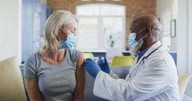 Oturma odasında maske takan yaşlı kadın ve doktor kanepede oturup aşı yapıyor. covid 19 salgını sırasında üst düzey sağlık ve yaşam tarzı.