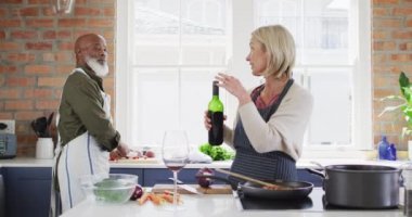 Kafkas kıdemli kadın önlük giyip evdeki mutfakta bir bardağa şarap dolduruyor. emekli çift yaşam tarzı konsepti