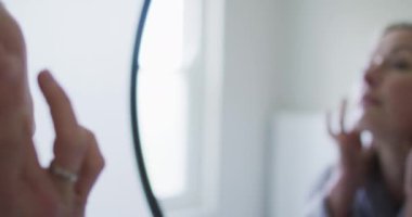 Banyodaki son sınıf beyaz kadın aynaya bakıyor, yüzüne dokunuyor. emeklilik yaşam tarzı, evde zaman geçirme..