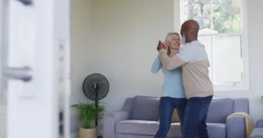 Karışık ırk son sınıf çifti evdeki oturma odasında dans ediyor. emekli çift yaşam tarzı konsepti