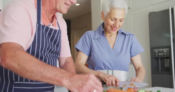 台所で一緒に調理するエプロンを身に着けて幸せな白人のシニアカップルのアニメーション 積極的で健康的な退職生活を送っています — ストック動画