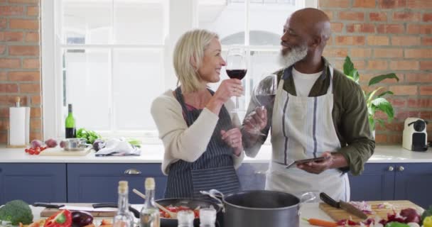 Casal Sênior Corrida Mista Usando Aventais Bebendo Vinho Enquanto Cozinha — Vídeo de Stock