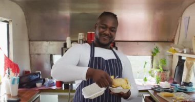 Gülümseyen Afro-Amerikan erkek işyeri sahibi yemek kamyonunda yemek hazırlıyor. Küçük bağımsız işletme, sokak yemekleri, servis ve catering.