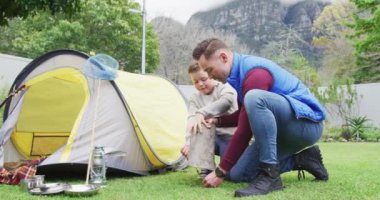 Oğlu bahçesinde çadır olan mutlu beyaz bir baba ve kamp kuruyor. Aile evde vakit geçiriyor..