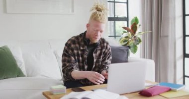 Albino Afro-Afrikalı Amerikalı. Rasta saçlı ve dizüstü bilgisayar kullanan bir adam. Uzaktan kumanda evde teknoloji kullanarak çalışıyor.
