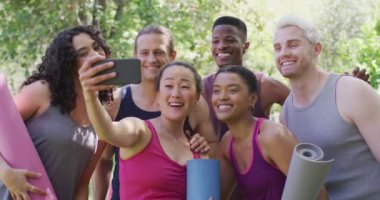 Yoga minderleri tutan bir grup genç parkta selfie çekiyor. yoga, meditasyon ve sağlıklı yaşam tarzı konsepti