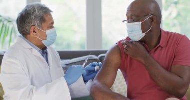Yüz maskesi takan erkek doktor evde Afrika kökenli Amerikalı son sınıf öğrencisi aşılıyor. Koronavirüs salgınının önlenmesi için aşı