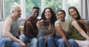 Aşılanmış omuzlarını gösteren ve evde selfie çeken bir grup genç insan. Koronavirüs salgınının önlenmesi için aşı