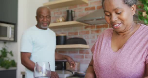 幸せなアフリカ系アメリカ人の高齢者のカップルのキッチンでワインを飲む リラックスして家で過ごす退職生活 — ストック動画