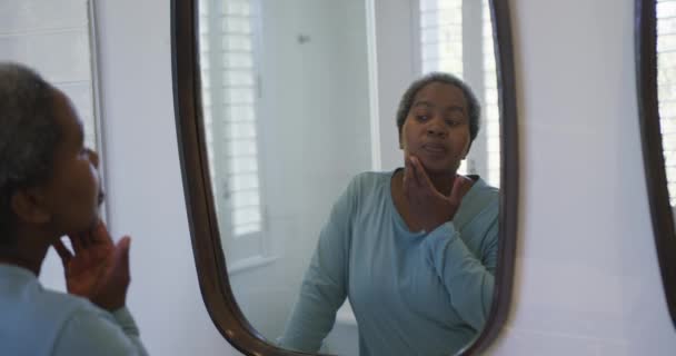 アフリカ系アメリカ人の年配の女性が浴室で鏡を見ている 退職生活やリラックスして家で過ごす時間 — ストック動画