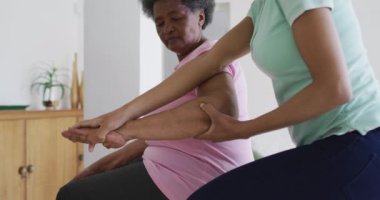 Yüz maskesi takan Afrika kökenli Amerikalı kadın fizyoterapist yaşlı kadın hasta egzersizlerine yardım ediyor. Üst düzey sağlık ve tıbbi fizyoterapi tedavileri, covid 19 salgını sırasında.