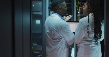 İş sunucu odasında çalışan Afrikalı Amerikalı bilgisayar teknisyenleri dizüstü bilgisayar kullanıyor. dijital bilgi depolama ve iletişim ağı teknolojisi.