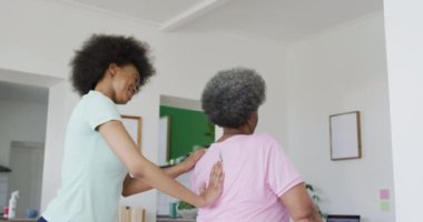 Yüz maskesi takan Afrika kökenli Amerikalı kadın fizyoterapist yaşlı kadın hasta egzersizlerine yardım ediyor. Üst düzey sağlık ve tıbbi fizyoterapi tedavileri, covid 19 salgını sırasında.