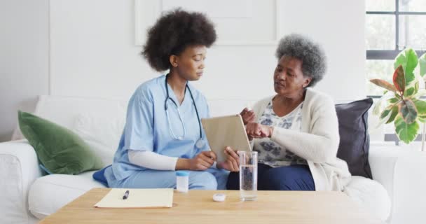 Afroamerikansk Kvinnlig Läkare Och Äldre Kvinna Pratar Och Använder Tabletter — Stockvideo
