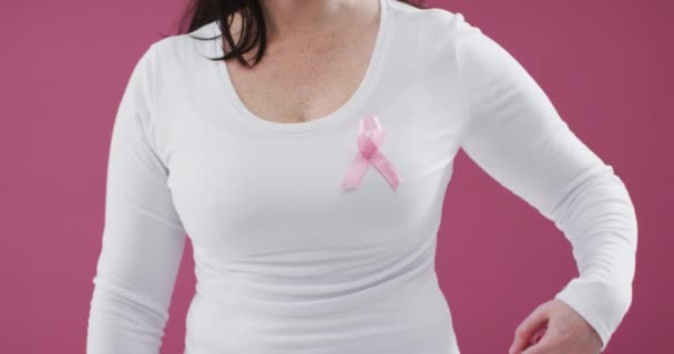 一个女人的中间部分指向她胸前的粉色缎带 衬托着粉色背景 乳腺癌意识概念 — 图库视频影像