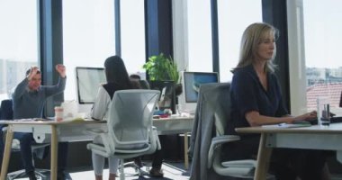 Kafkasyalı iş adamının modern bir ofiste çalıştığını, masasının başında durup, elleri havada tezahürat yaptığını, meslektaşlarının yavaş çekimde masalarında çalıştığını.