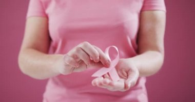 Pembe arka planda pembe kurdele tutan bir kadının orta bölümü. Göğüs kanseri farkındalığı kavramı