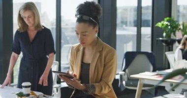 Modern bir ofiste çalışan melez bir kadının ön görüntüsü, tablet bilgisayar kullanıyor, arka planda çalışan meslektaşları, yavaş çekim.