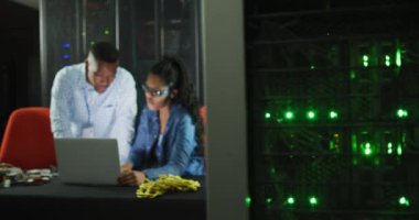 İş sunucu odasında çalışan Afrikalı Amerikalı bilgisayar teknisyenleri dizüstü bilgisayar kullanıyor. dijital bilgi depolama ve iletişim ağı teknolojisi.