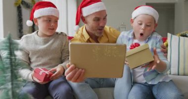 Kafkasyalı baba ve iki oğlu Noel 'de dijital tablet üzerinde video görüşmesi yaparak hediyelerini açıyorlar. Noel zamanı covid 19 salgınında sosyal mesafeler