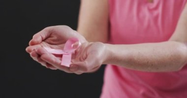 Siyah arka planda pembe kurdele tutan bir kadının orta bölümü. Göğüs kanseri farkındalığı kavramı