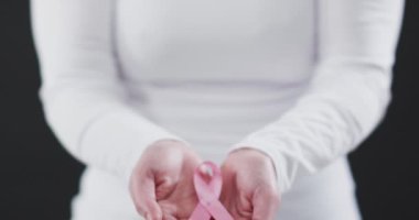 Siyah arka planda pembe kurdele tutan bir kadının orta bölümü. Göğüs kanseri farkındalığı kavramı