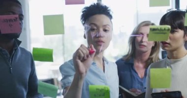 Modern bir ofiste çalışan çeşitli iş adamlarının ön görüşü. Yavaş çekimde görülen notlarla tahtada beyin fırtınası yapıyorlar.