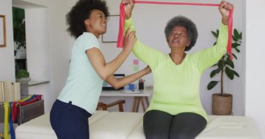 Mutlu Afro-Amerikan kadın fizyoterapist yaşlı kadın hastaların evde egzersiz yapmasına yardım ediyor. Üst düzey sağlık ve tıbbi fizyoterapi tedavisi.