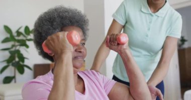 Mutlu Afro-Amerikan kadın fizyoterapist yaşlı kadın hastaların evde egzersiz yapmasına yardım ediyor. Üst düzey sağlık ve tıbbi fizyoterapi tedavisi.