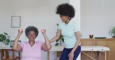 Mutlu Afro-Amerikan kadın fizyoterapist yaşlı kadın hastaların evde egzersiz yapmasına yardım ediyor. Üst düzey sağlık ve tıbbi fizyoterapi tedavisi.