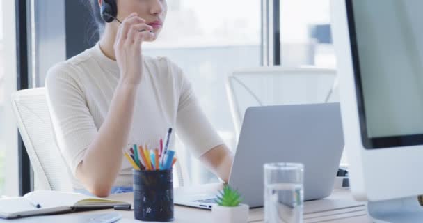 一个快乐的混血女商人在现代化的办公室里工作 使用笔记本电脑 头戴耳机 慢动作的侧视图 — 图库视频影像