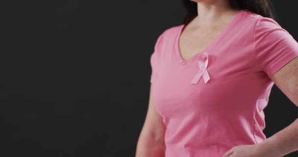 黒を背景に胸にピンクのリボンを指差す女性のミッドセクション 乳がんの認知概念は — ストック動画