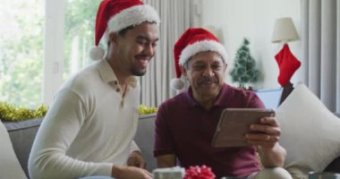 Noel Baba şapkalı neşeli çift ırklı oğlu Noel 'de tablet bilgisayardan video görüşmesi yapıyor. Noel, şenlik ve iletişim teknolojisi.
