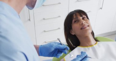 Modern diş kliniğinde kadın hastaların dişlerini inceleyen yüz maskeli beyaz erkek diş hekimi. covid 19 salgını sırasında sağlık ve dişçilik sektörü.