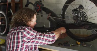 Garajdaki aletleri kullanarak bisiklet tamir etmeye odaklanmış beyaz bir adam. Yurtiçi yaşam tarzı, evdeki iletişim teknolojisini kullanarak..