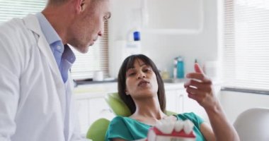 Modern diş kliniğindeki kadın hastaların dişlerini inceleyen beyaz erkek dişçi. Sağlık ve dişçilik sektörü.