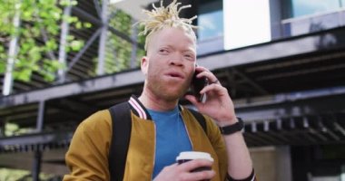 Mutlu albino Afro-Amerikan adam elinde rasta ile kahve içerek akıllı telefondan konuşuyor. Dijital göçebe şehirde geziyor, dolaşıyor..