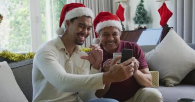 Noel Baba şapkalı baba ile mutlu çift ırklı oğul Noel 'de akıllı telefondan video görüşmesi yapıyor. Noel, şenlik ve iletişim teknolojisi.
