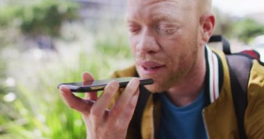 Parkta rastalı saçlı, akıllı telefondan konuşan mutlu albino Afrikalı Amerikalı adam. Dijital göçebe şehirde geziyor, dolaşıyor..